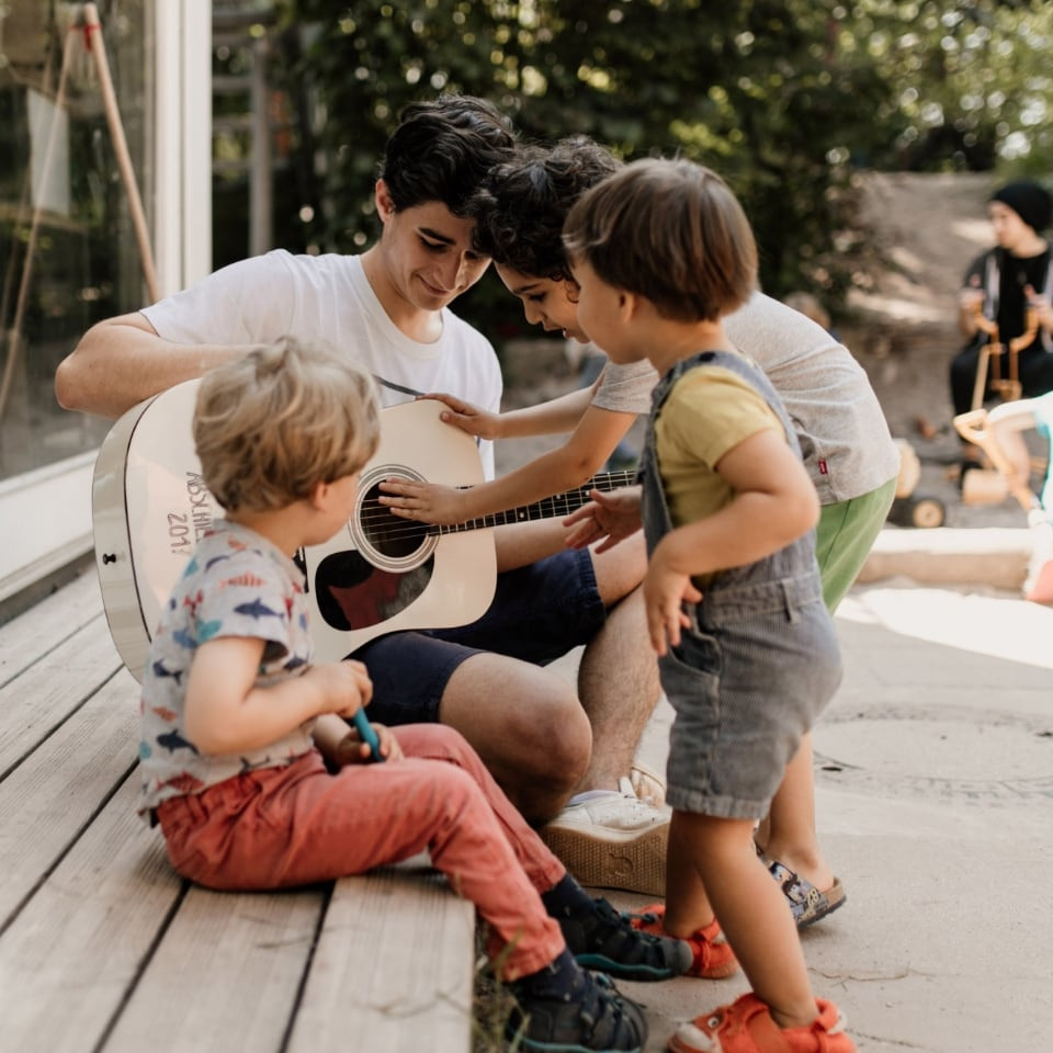 Ein Erzieher spielt den Kindern auf der Terrasse Gitarre vor