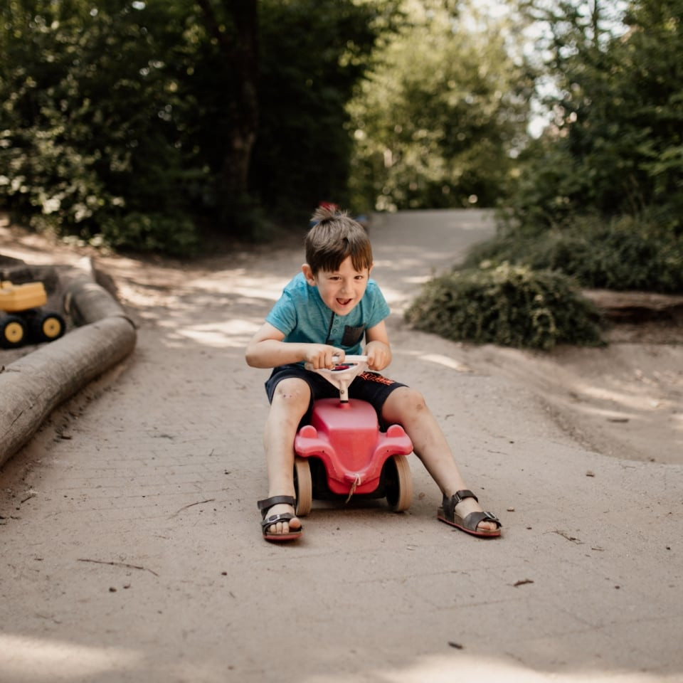 Ein Kind fährt mit einem roten Rutschauto über den Weg im Garten