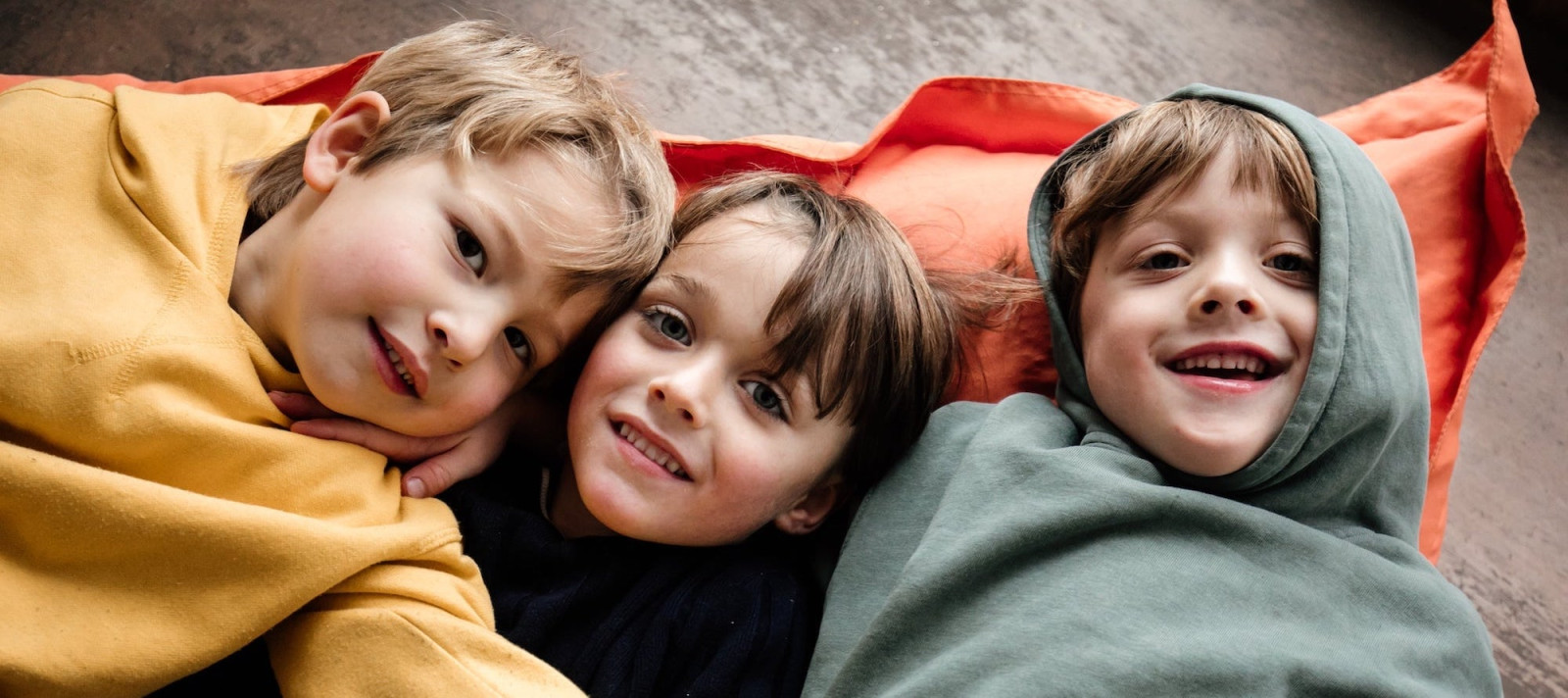 Drei Kinder kuscheln sich lachend unter Decken