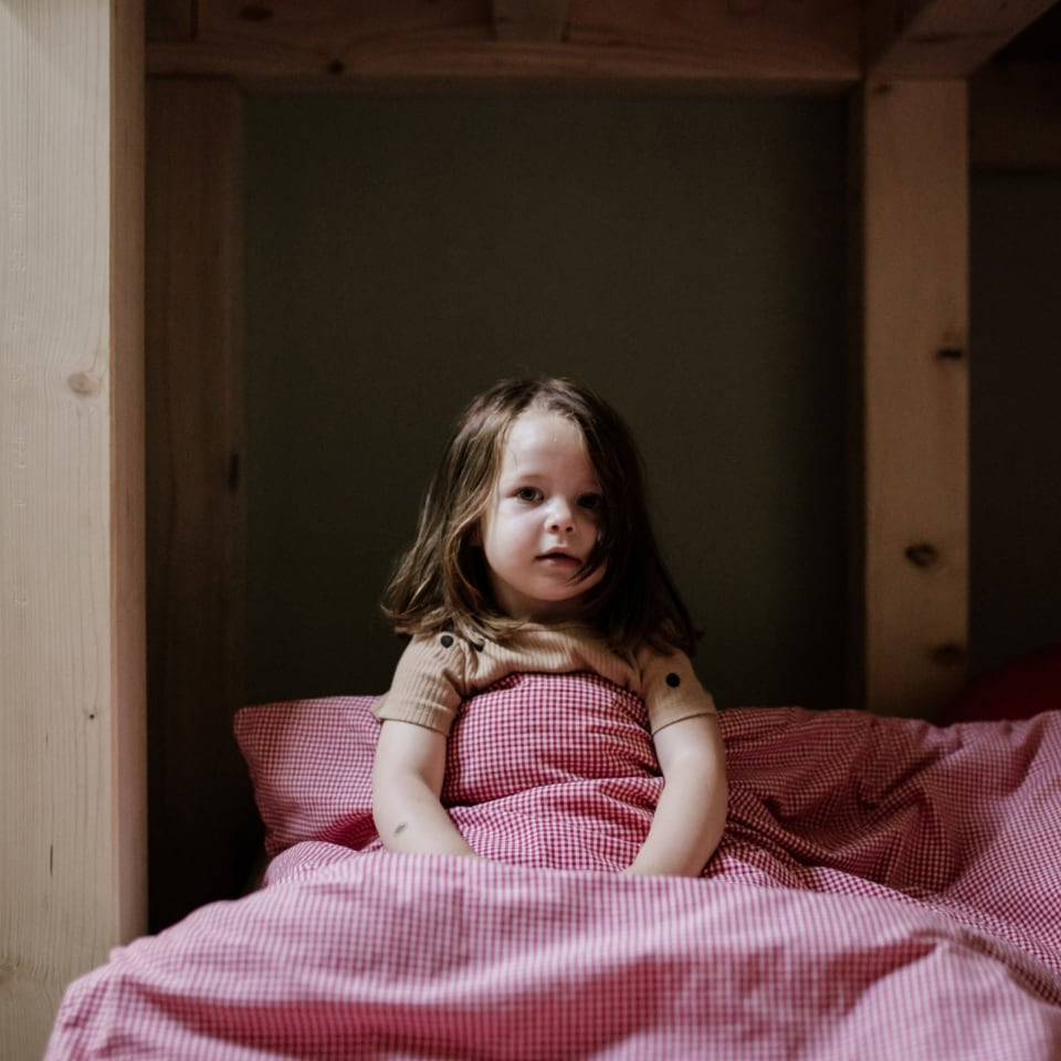 Ein Kind sitzt im Bett unter einer rosa Decke
