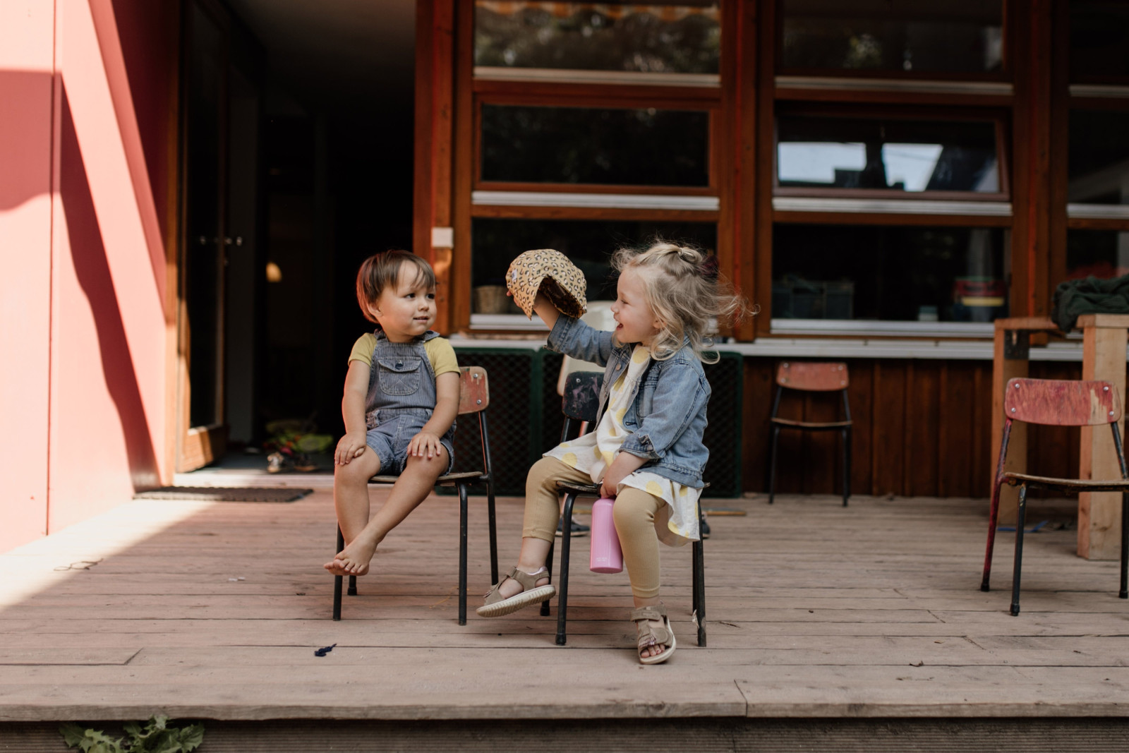 Zwei Kleinkinder sitzen auf Stühlen vor dem Haus