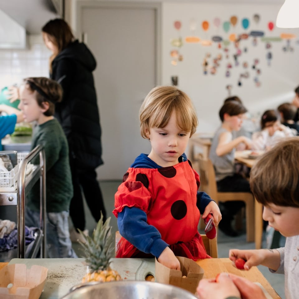 Kinder schneiden mit einer Erzieherin in der Küche Obst