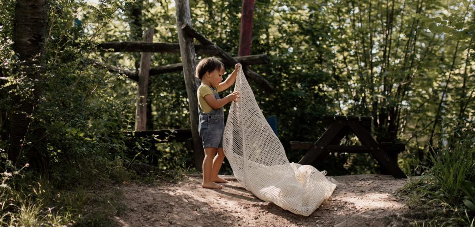 Ein Kind spielt mit einem Tuch im Garten unter den Bäumen
