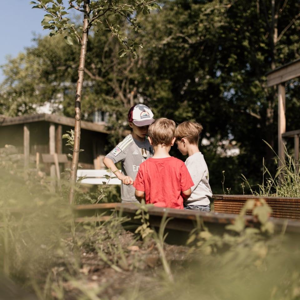 Kinder und ein Betreuer im Garten am Hochbeet