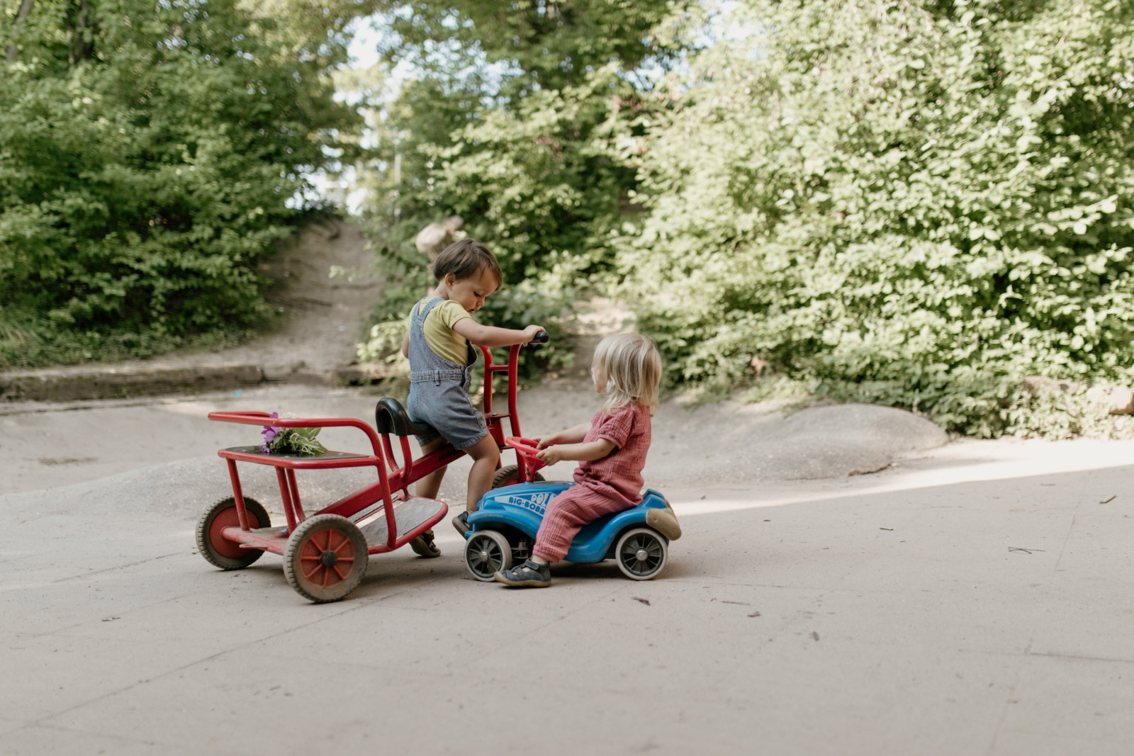 Zwei Kinder mit Rutschfahrzeugen auf dem Weg im Garten