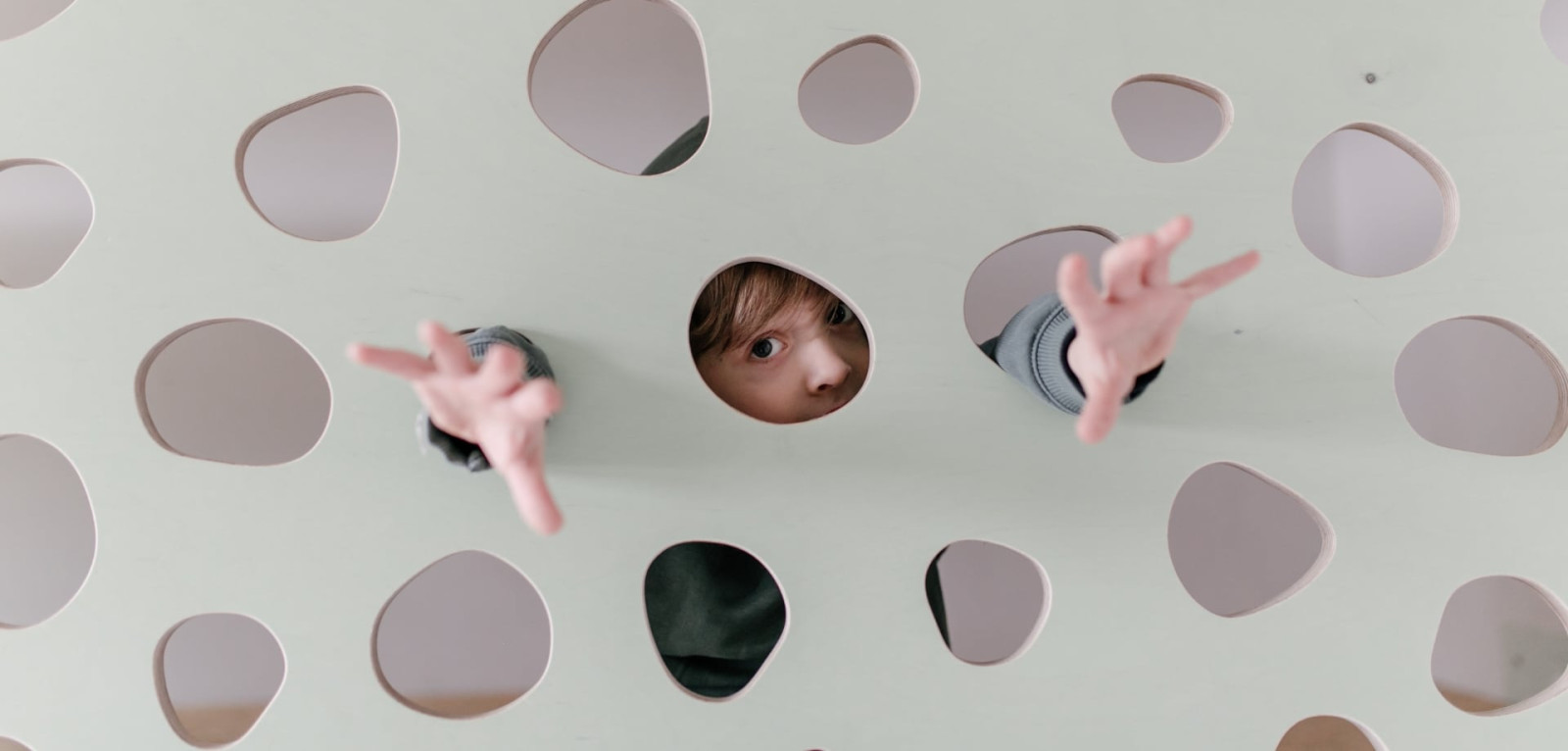 Kinder schauen durch die Löcher einer Spielwand